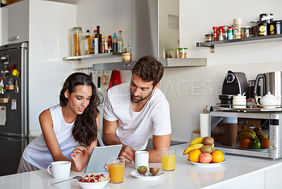 Buy stock photo Shot of a young couple using a digital tablet together during their morning routine at home