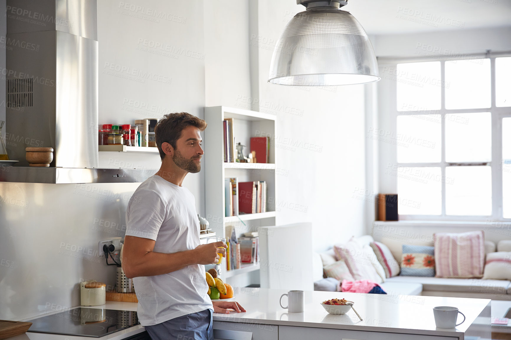 Buy stock photo Shot of a handsome young man drinking juice in the morning at home and looking thoughtful