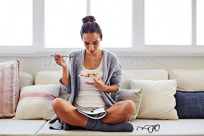 Buy stock photo Shot of a beautiful young woman going over some work while having breakfast in the morning at home