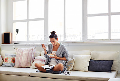 Buy stock photo Shot of a beautiful young woman going over some work while having breakfast in the morning at home