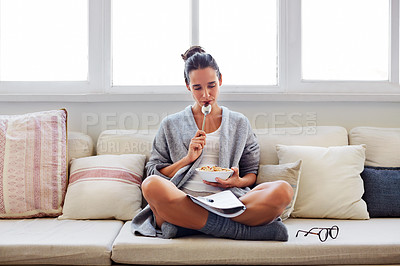 Buy stock photo Shot of a beautiful young woman going over some work while having breakfast in the morning at home