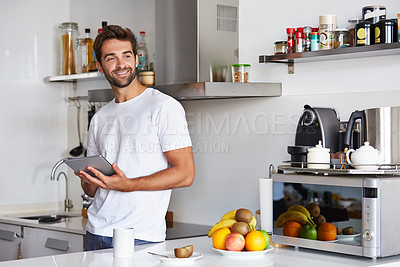 Buy stock photo Shot of a handsome young man using a digital tablet in the morning at home