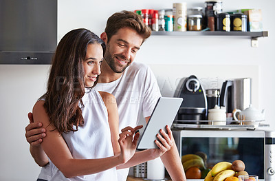 Buy stock photo Shot of a young couple using a digital tablet together during their morning routine at home