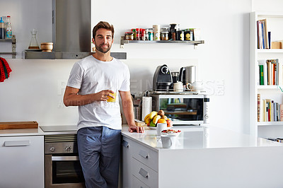 Buy stock photo Shot of a handsome young man drinking juice in the morning at home and looking thoughtful