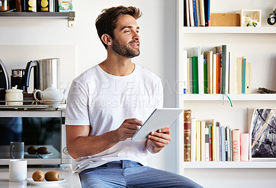 Buy stock photo Shot of a handsome young man using a digital tablet in the morning at home