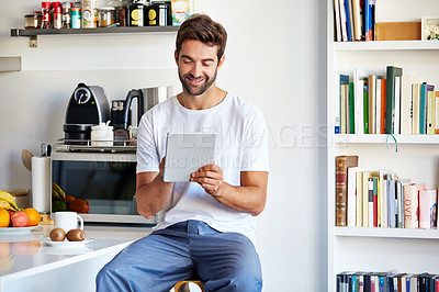 Buy stock photo Shot of a handsome young man using a digital tablet in the morning at home