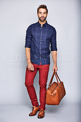 Buy stock photo Studio portrait of a handsome young man carrying a suitcase against a grey background