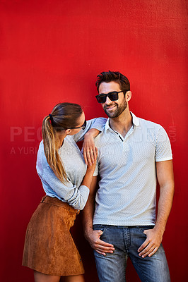 Buy stock photo Shot of a fashionable young couple leaning against a red wall outside