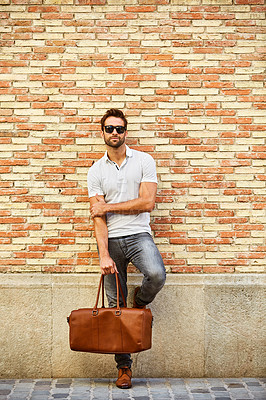 Buy stock photo Shot of a fashionable young man leaning against a brick wall outside