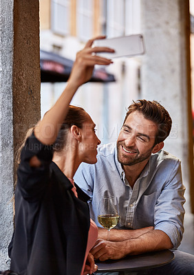 Buy stock photo Shot of a happy couple taking a selfie while sitting outside at a restaurant