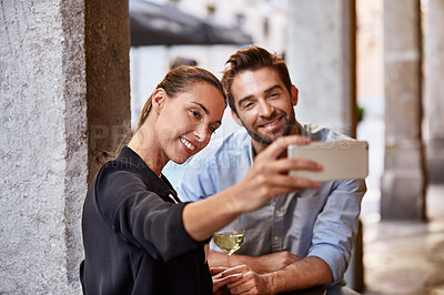 Buy stock photo Shot of a happy couple taking a selfie while sitting outside at a restaurant