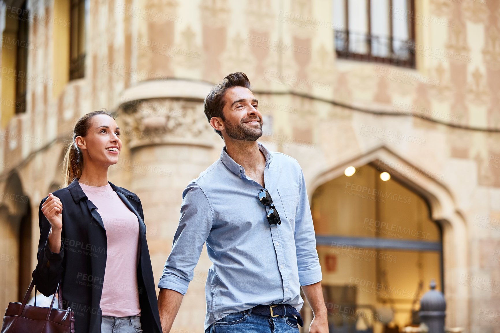 Buy stock photo Shot of an affectionate young couple walking hand in hand together in the city