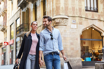 Buy stock photo Shot of an affectionate young couple walking hand in hand together in the city