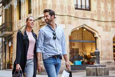 Buy stock photo Shot of an affectionate young couple walking hand in hand together in the city