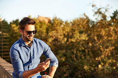 Buy stock photo Shot of a man using his cellphone while sitting on a rooftop