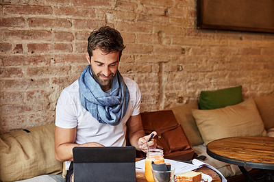 Buy stock photo Shot of a handsome young man using his digital tablet while sitting in a cafe