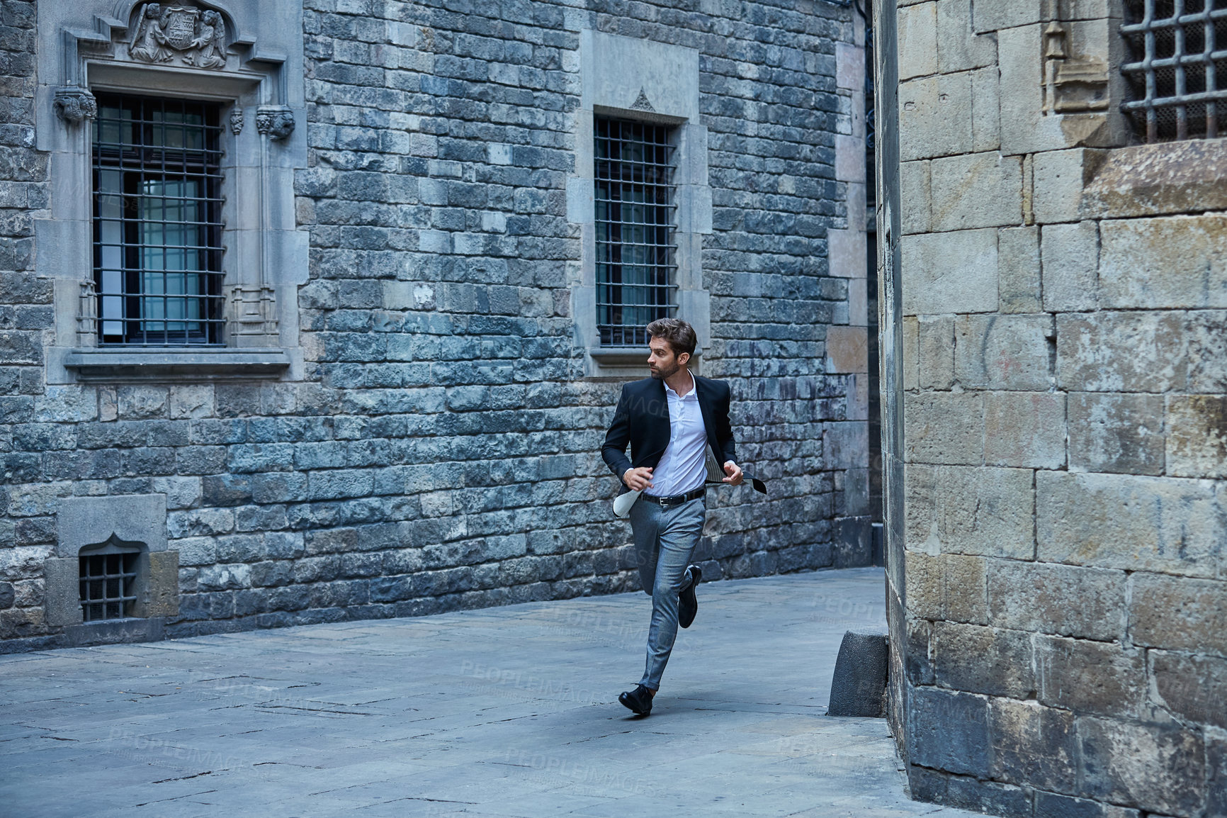 Buy stock photo Full length shot of a handsome young businessman running through an urban alleyway