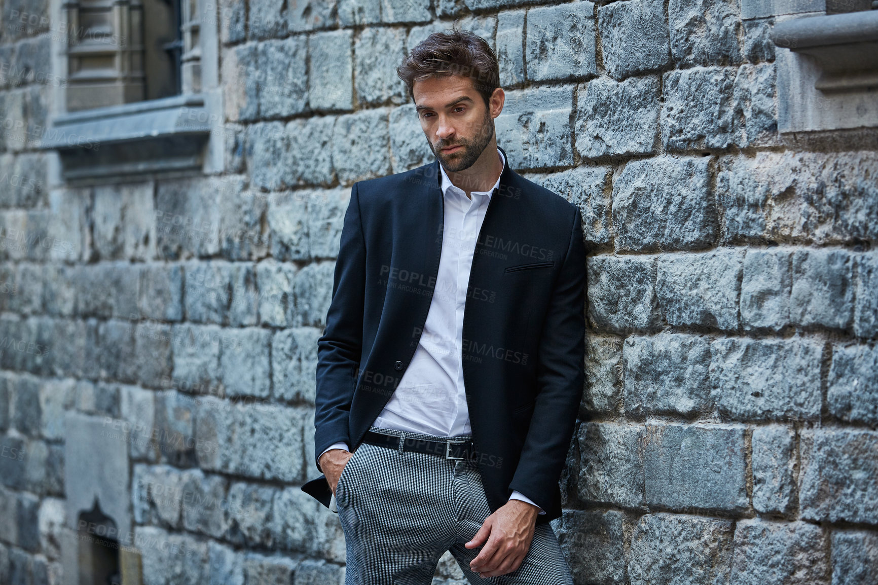 Buy stock photo Cropped shot of a handsome young businessman standing against a brick wall in an urban alleyway
