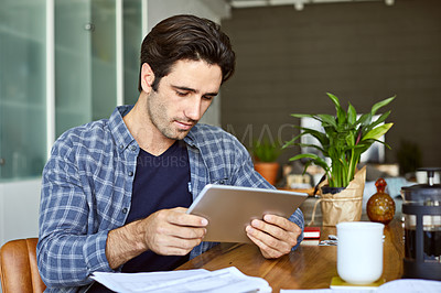 Buy stock photo Cropped shot of a handsome young man using a tablet while working from home
