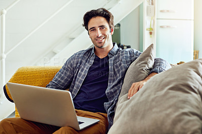 Buy stock photo Portrait of a cheerful young man working on a laptop while being seated on a couch at home