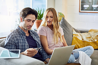 Buy stock photo Shot of a focused young couple working together on a laptop while being seated on a couch at home