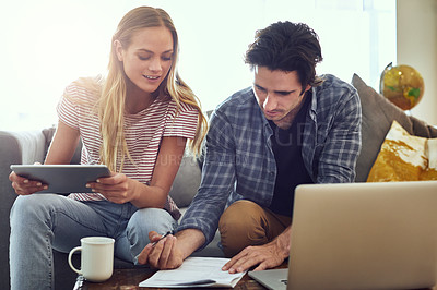 Buy stock photo Shot of a cheerful young couple working together on a digital tablet while being seated on a couch at home