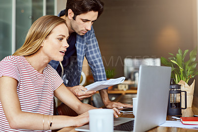 Buy stock photo Shot of a focused young couple working together on a laptop while being seated next to table at home