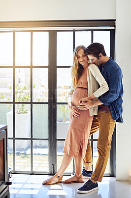 Buy stock photo Shot of a young man embracing his pregnant wife at home
