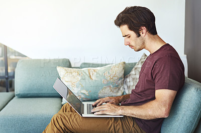 Buy stock photo Shot of a handsome young man using his laptop on the sofa at home