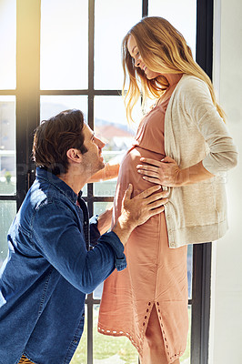 Buy stock photo Shot of a young man feeling his pregnant wife's tummy at home