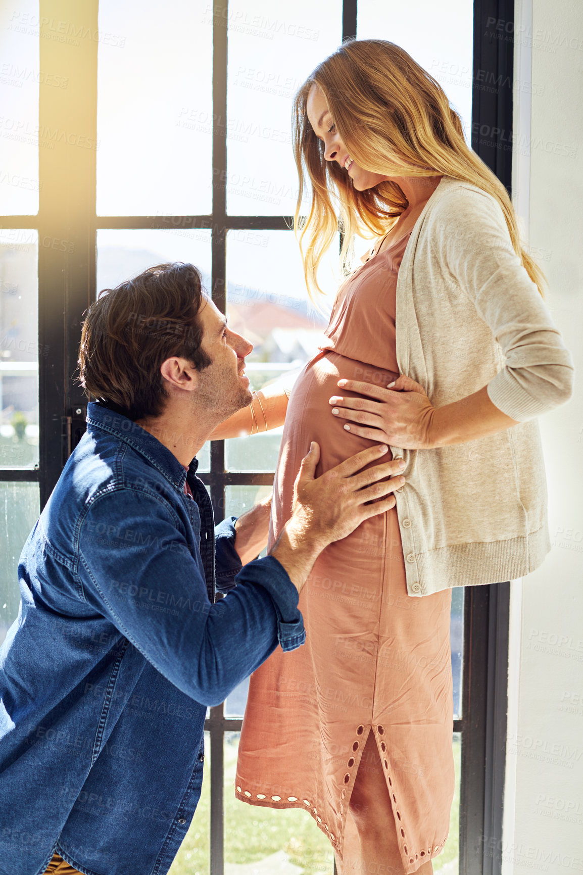 Buy stock photo Shot of a young man feeling his pregnant wife's tummy at home