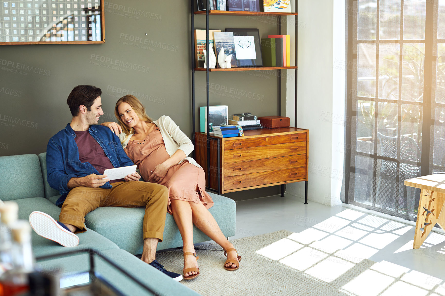Buy stock photo Happy, couple and pregnant woman in home with tablet, internet connection and research for baby name. People, smile and relax in lounge with relationship, pregnancy and tech for family planning.