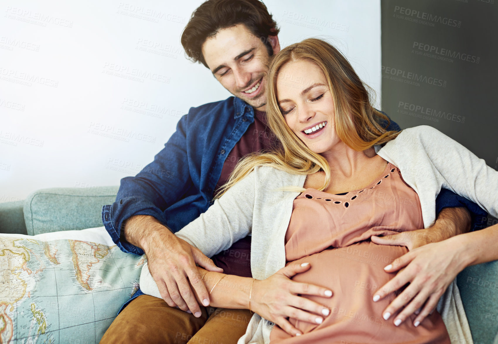 Buy stock photo Shot of a young man relaxing with his pregnant wife on the sofa at home