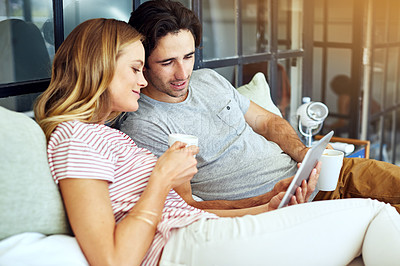 Buy stock photo Shot of a young couple using a digital tablet together while relaxing on the sofa at home