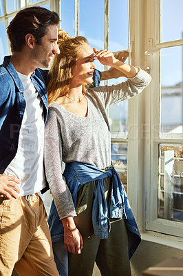 Buy stock photo Shot of a young couple looking out of the window at home