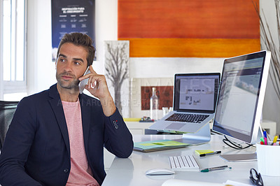 Buy stock photo Shot of a young businessman talking on his phone while sitting at his desk