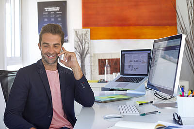 Buy stock photo Shot of a young businessman talking on his phone while sitting at his desk