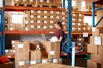 Buy stock photo Shot of a young woman using a laptop in a warehouse