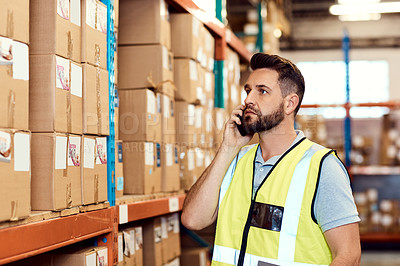 Buy stock photo Shot of a young man talking on a cellphone while working in a warehouse