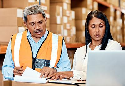 Buy stock photo Shot of a mature man and woman going through paperwork while using a laptop in a warehouse
