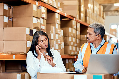 Buy stock photo Shot of a woman making a phone call while working with a colleague in a warehouse