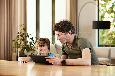Buy stock photo Shot of a cute little boy using a digital tablet with his father at home