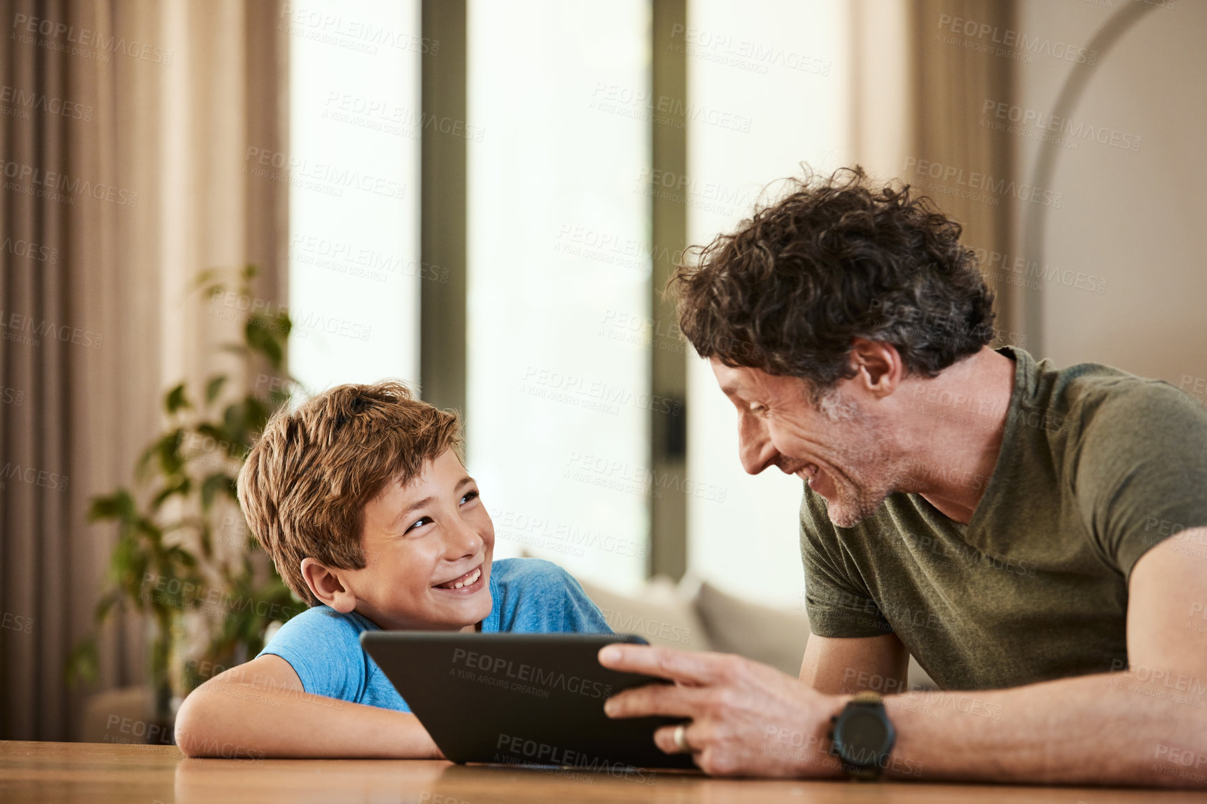 Buy stock photo Shot of a cute little boy using a digital tablet with his father at home