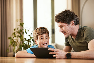 Buy stock photo Shot of a cute little boy using a digital tablet with his father at home