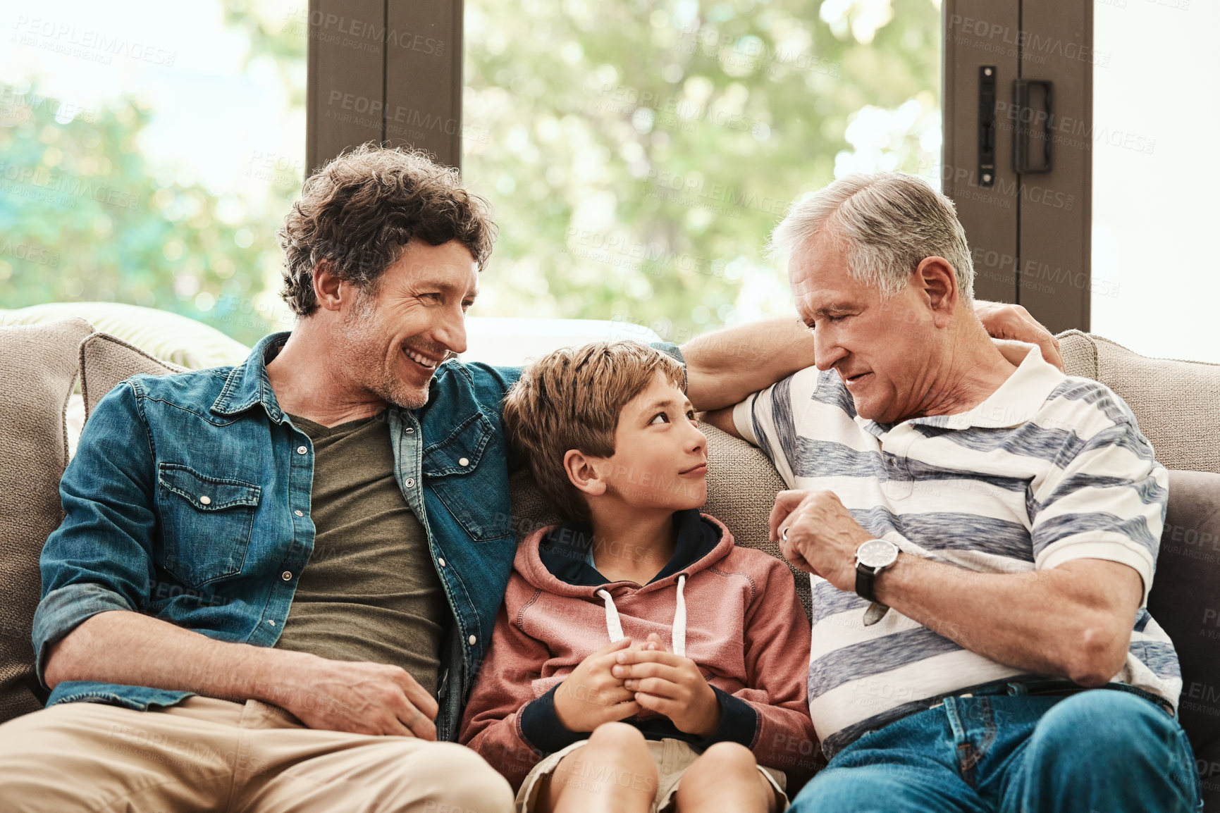 Buy stock photo Shot of an adorable little boy relaxing on the sofa with his father and grandfather at home