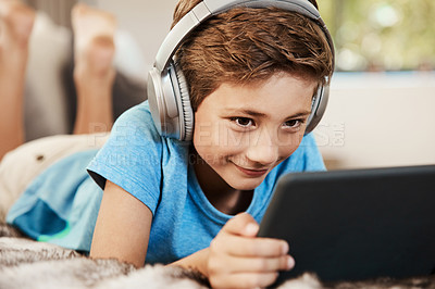 Buy stock photo Shot of a cute little boy using a digital tablet with headphones on the sofa at home