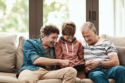 Buy stock photo Shot of a little boy using a digital tablet with his father and grandfather at home