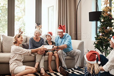 Buy stock photo Shot of a cheerful family opening presents together while being seated on a sofa during Christmas time