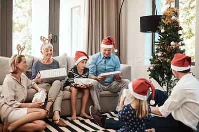 Buy stock photo Shot of a cheerful family opening presents together while being seated on a sofa during Christmas time