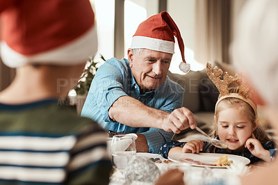 Buy stock photo Cropped shot of a cheerful elderly man dishing food into his granddaughter's plate at lunch during Christmas time